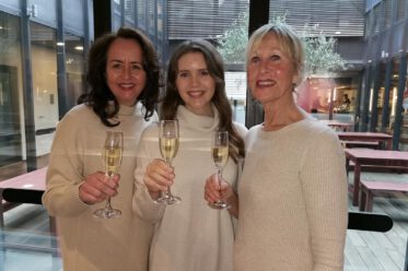 3 Frauen tragen helle Strickkleider und haben ein Sektglas in der Hand.